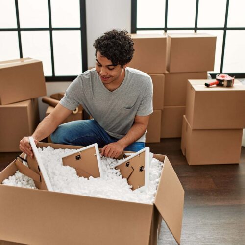 Young hispanic man smiling happy unboxing cardboard box at new home.