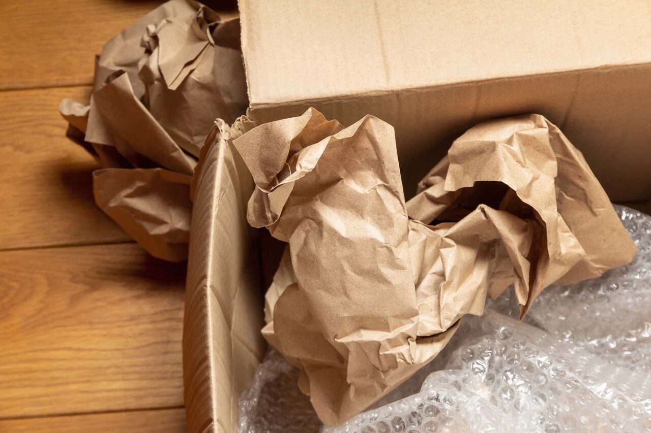 Opened cardboard box with crumpled wrapping paper and bubble wrap on wooden floor of room. The concept of storing, moving and sending goods and things