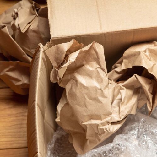 Opened cardboard box with crumpled wrapping paper and bubble wrap on wooden floor of room. The concept of storing, moving and sending goods and things