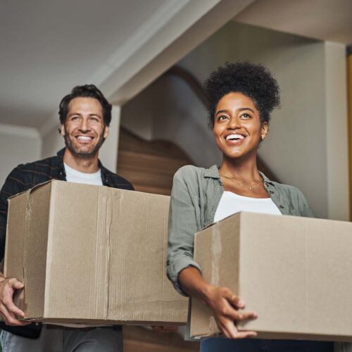 New house, moving and happy couple carrying boxes while feeling proud and excited about buying a house with a mortgage loan. Interracial husband and wife first time buyers unpacking in dream home.