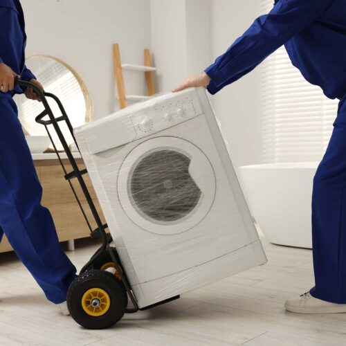 Male movers carrying washing machine in bathroom, closeup. New house