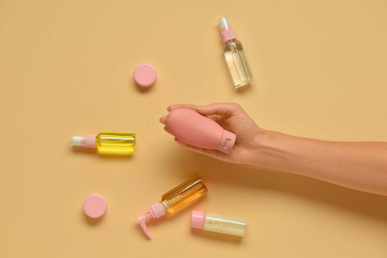 Female hand with with travel cosmetics kit on color background, closeup