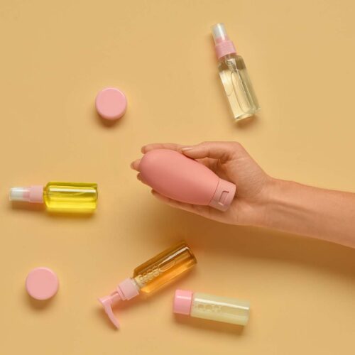 Female hand with with travel cosmetics kit on color background, closeup