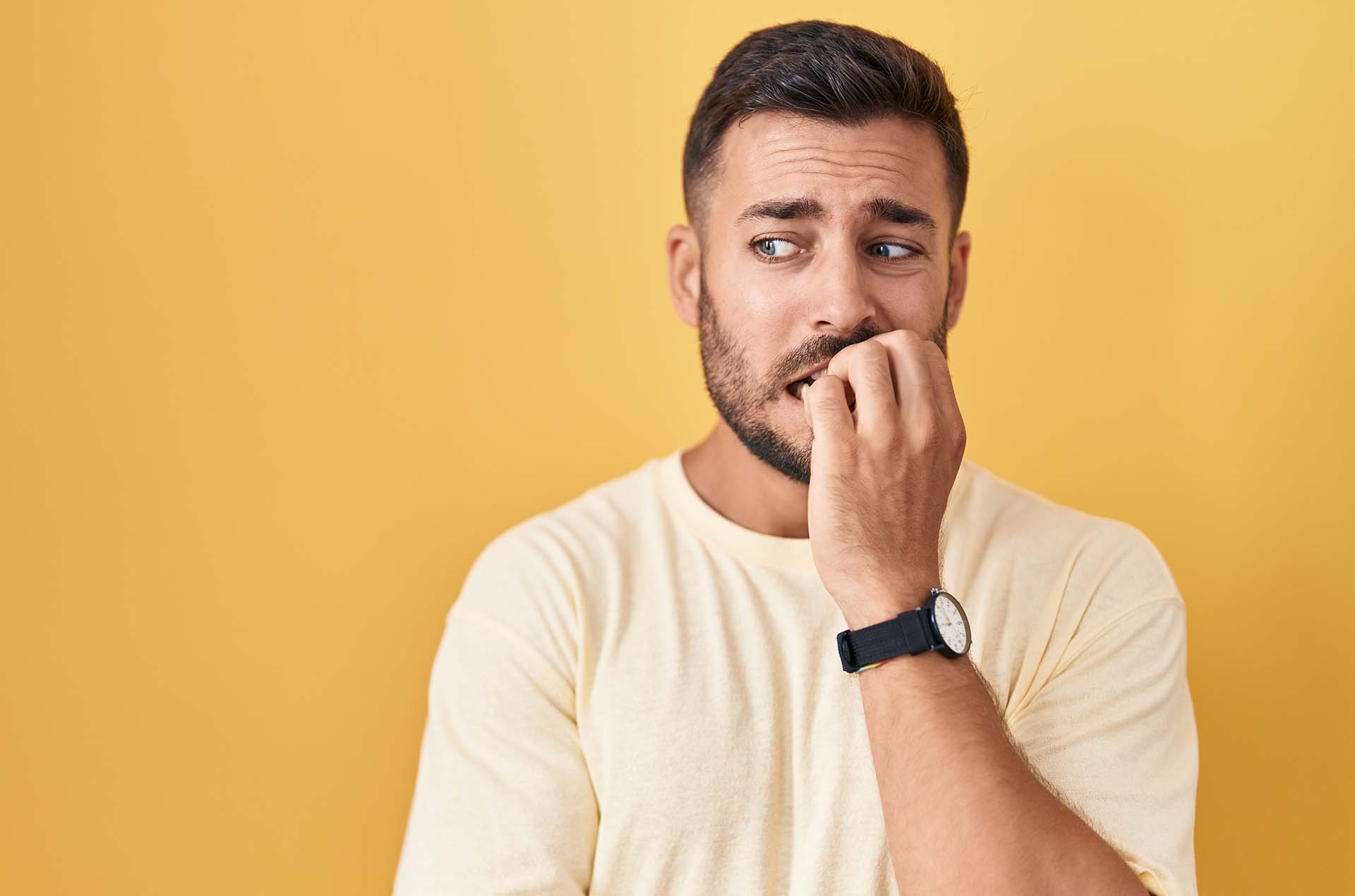 Handsome hispanic man standing over yellow background looking stressed and nervous with hands on mouth biting nails. anxiety problem.