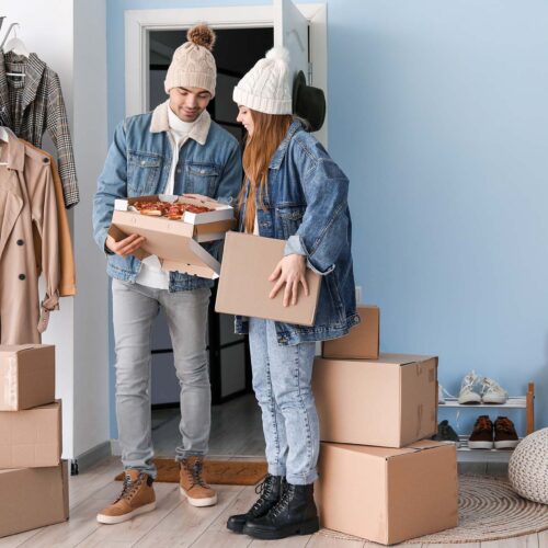 Happy young couple eating tasty pizza in hallway on moving day