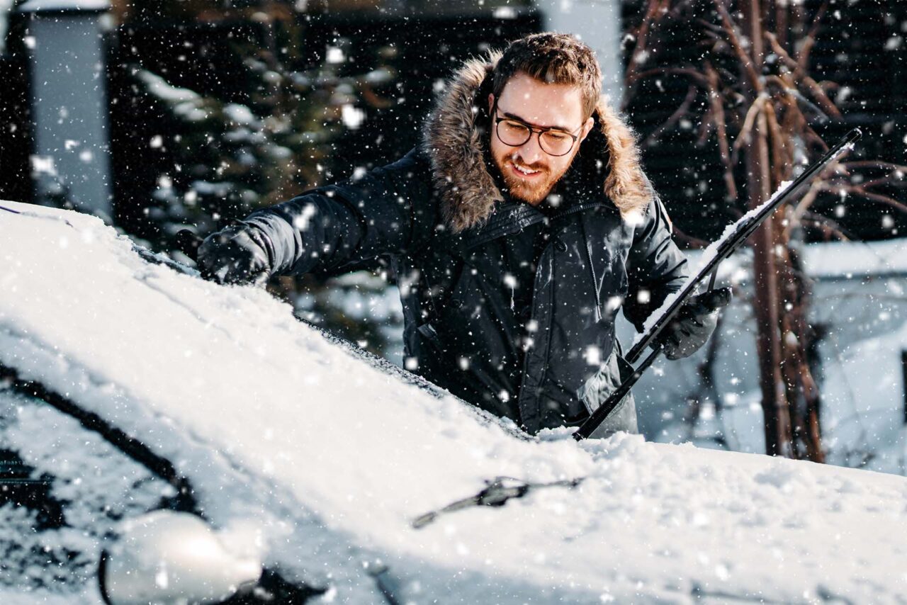 portrait of smiling man cleaning snow off his car during winter snowfall