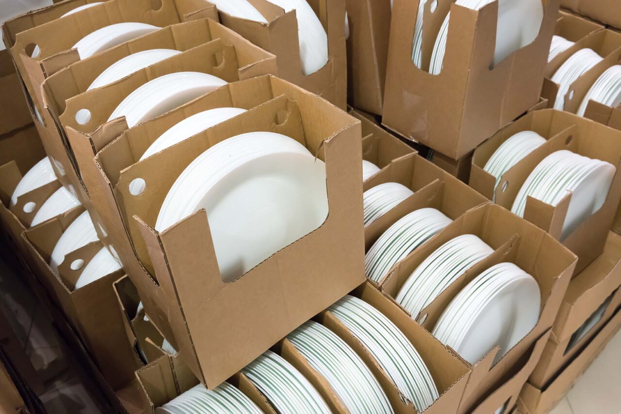 Stacks of white and round shaped porcelain plates in corrugated boxes.