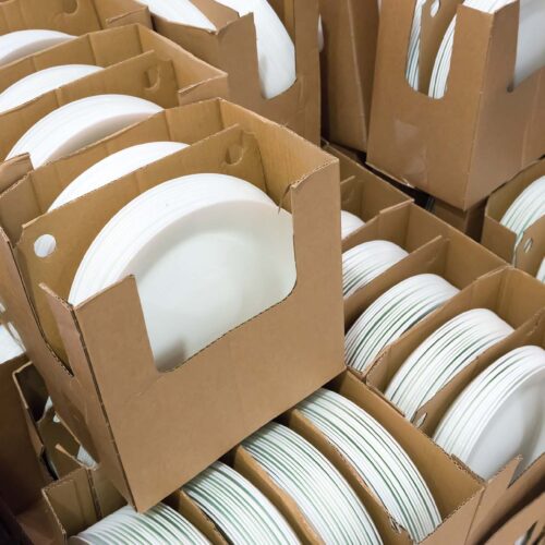 Stacks of white and round shaped porcelain plates in corrugated boxes.