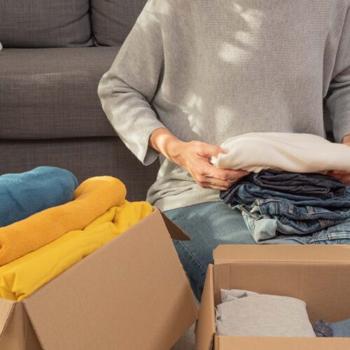 Woman sorting clothes and packing into cardboard box. Donations for charity, help low income families, declutter home, sell online, moving moving into new home, recycling, sustainable living concept.