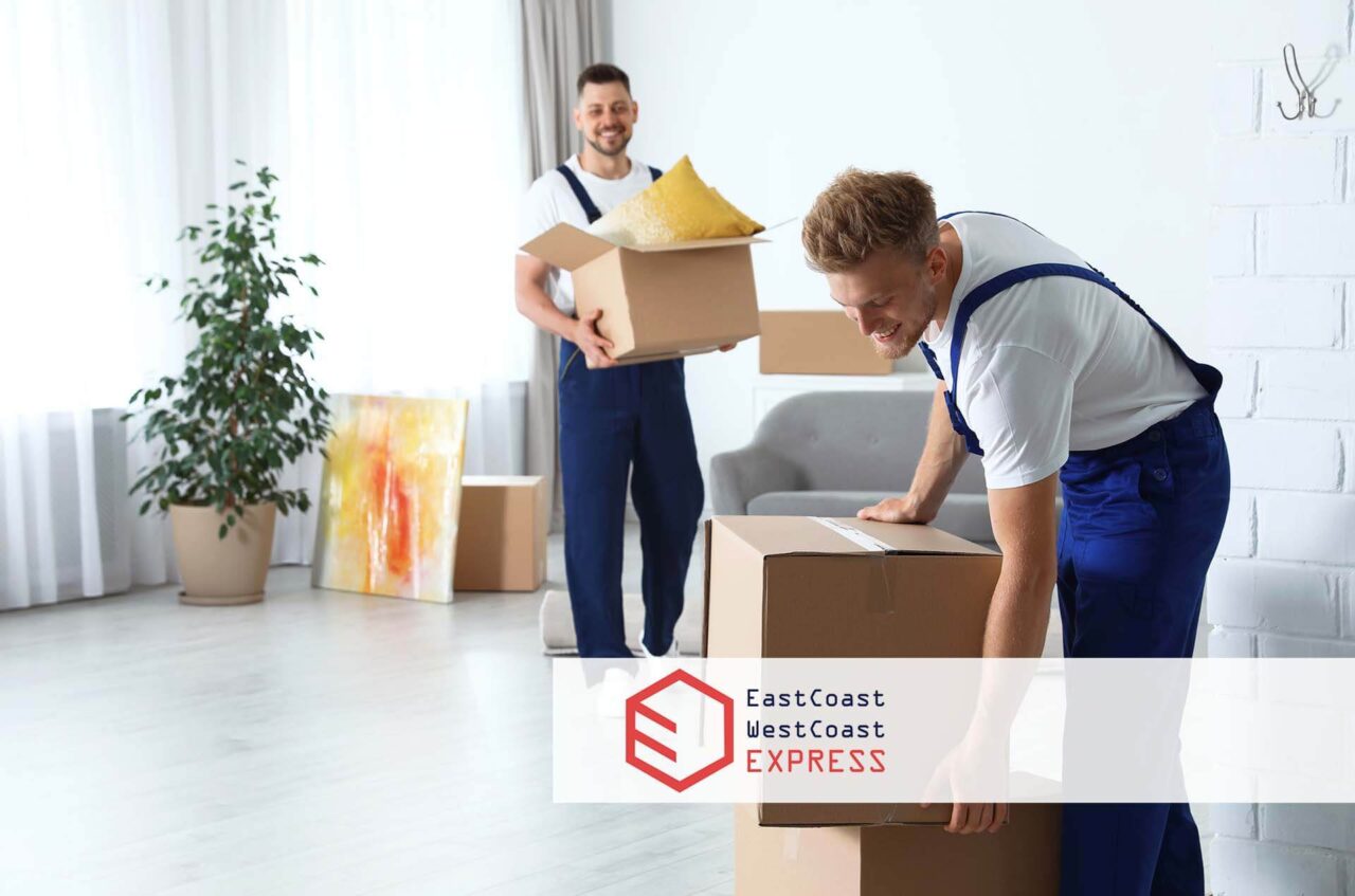 Two movers carrying boxes in a home East Coast West Coast Movers Logo
