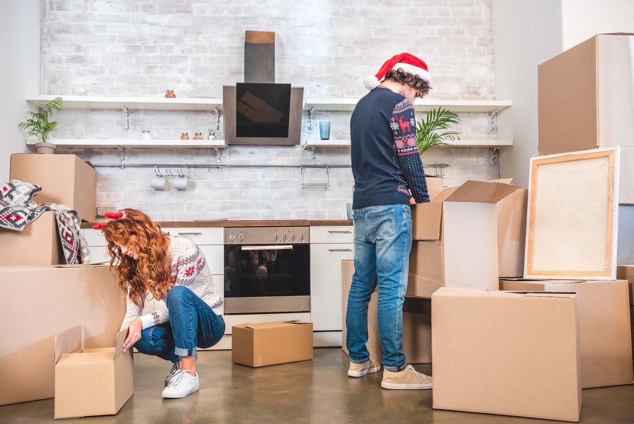 young couple unpacking cardboard boxes in new apartment at christmastime