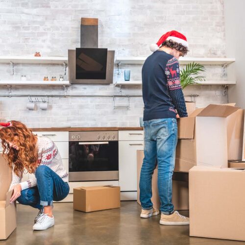 young couple unpacking cardboard boxes in new apartment at christmastime