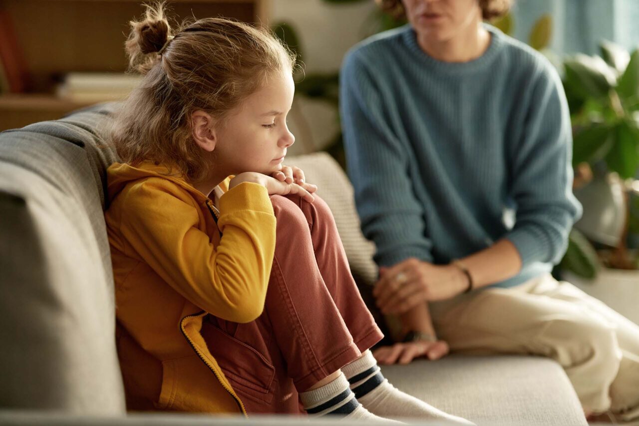 Little boy sitting on sofa without mood and having no desire to talk to his mom